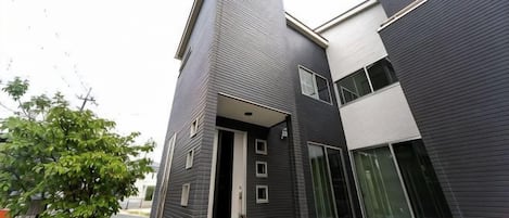 A modern two-story building with a dark exterior, a visible entrance, and a tiled ground floor.