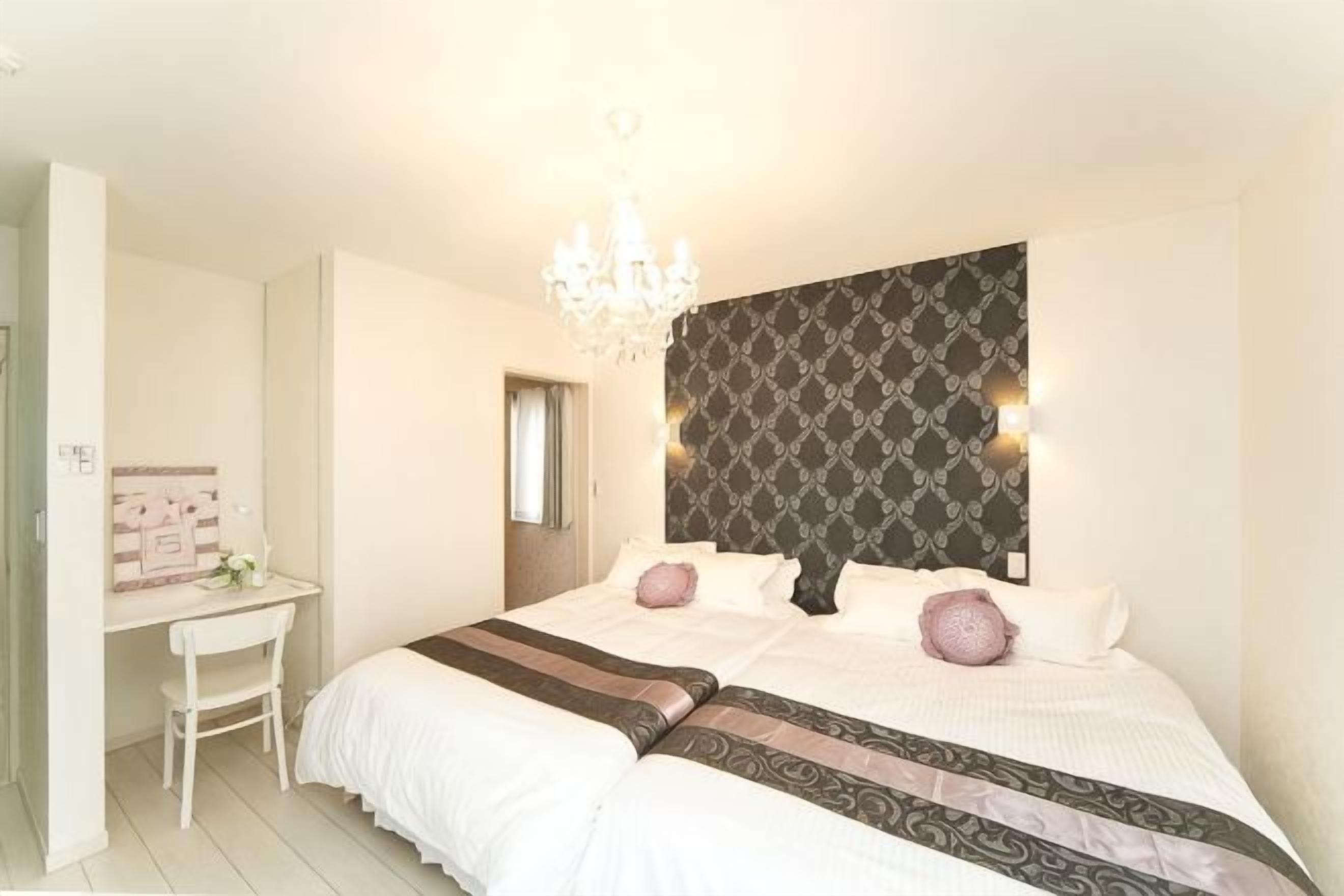 A bedroom with a large bed, a desk, and a chandelier.