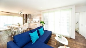 A modern living room with a blue sofa, a dining area, and a kitchen. - Shiga Lakeside Villa (Takashima)