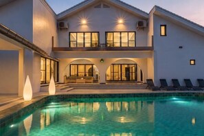 Une maison à deux étages avec une piscine, de grandes fenêtres et un balcon.