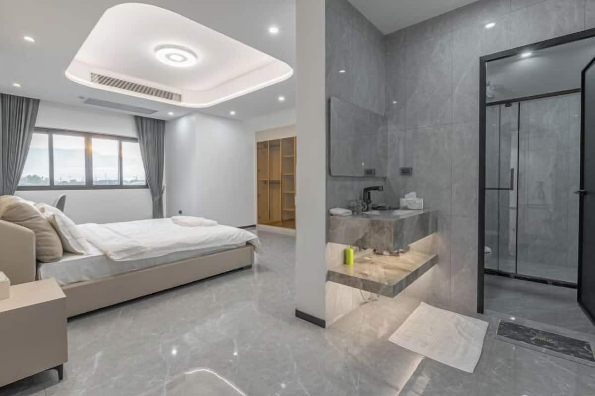 Ein modernes Hotelzimmer mit Bett, Nachttisch, Badezimmer mit Dusche und großem Fenster.