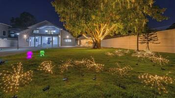 Um imóvel residencial à noite, com árvores iluminadas e uma casa bem iluminada.