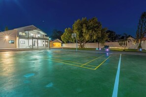 An outdoor basketball court at night with a building in the background.