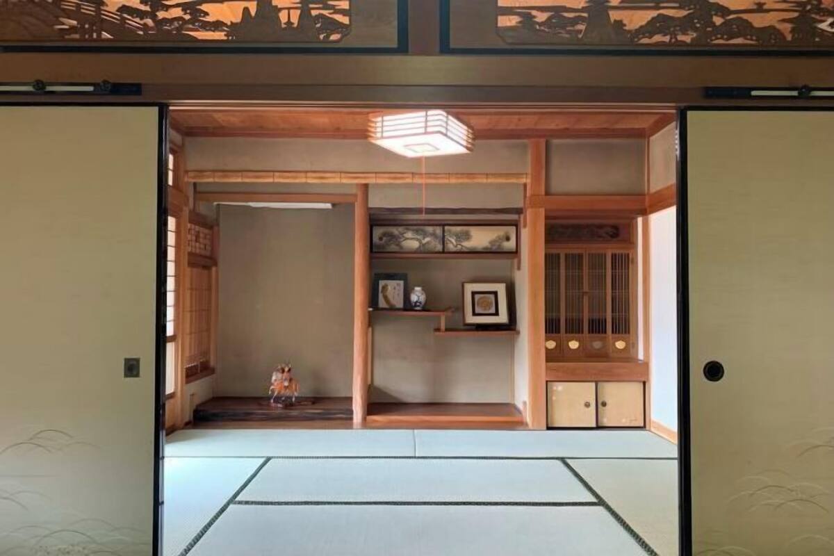 A traditional Japanese room with tatami flooring, a shoji screen door, a hanging lantern, and a small shelf with decorative items.