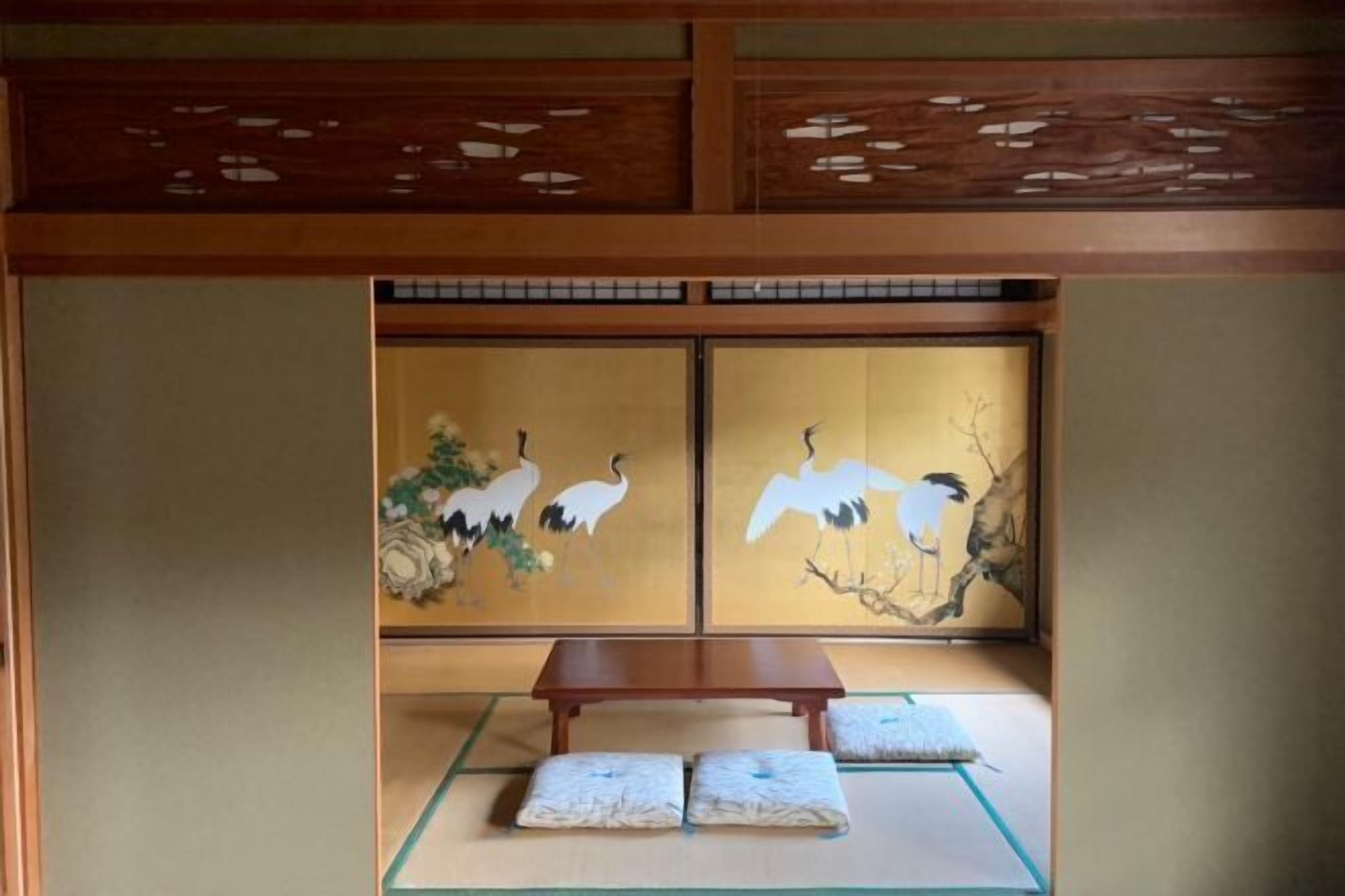 A traditional Japanese room with tatami flooring, a low wooden table, and sliding doors with crane paintings.