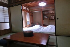 A traditional Japanese room with tatami flooring, a low wooden table, and a bed with white bedding. - Japanese inn yuasarou (Nantan)