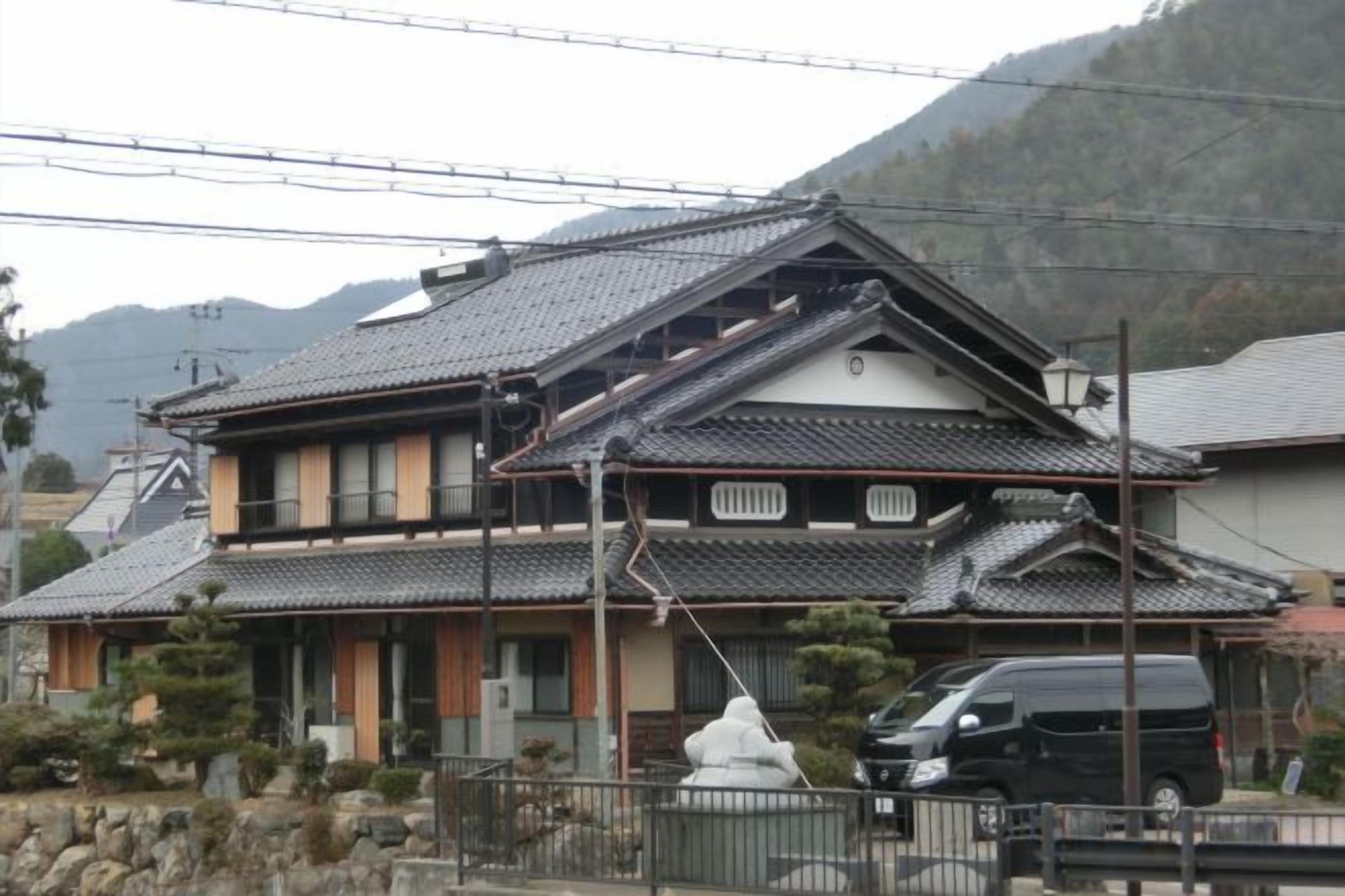 A traditional Japanese house with a tiled roof, a stone pathway, and a parked car.