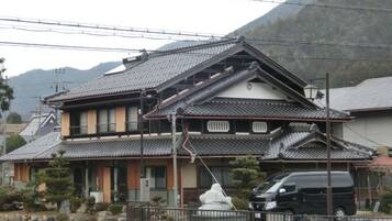 A traditional Japanese house with a tiled roof, a stone pathway, and a parked car.
