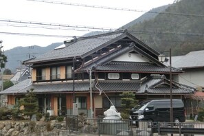 A traditional Japanese house with a tiled roof, a stone pathway, and a parked car. - Japanese inn yuasarou (Nantan)