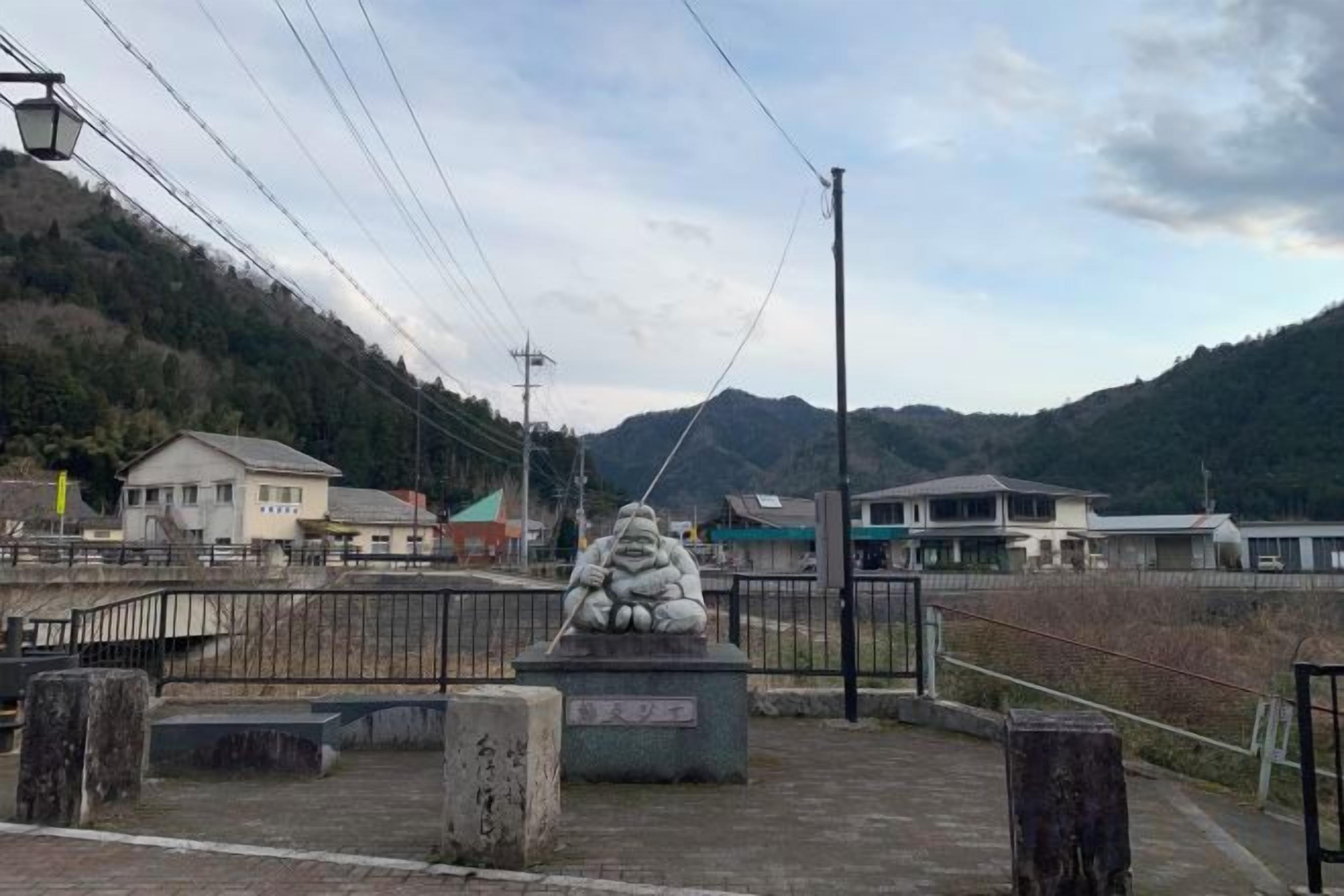 A stone statue in a fenced area with a view of a mountain and buildings in the background.