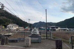 Une statue de pierre, située dans un espace délimité par une clôture, d’où l’on peut admirer une montagne et des bâtiments en arrière-plan.