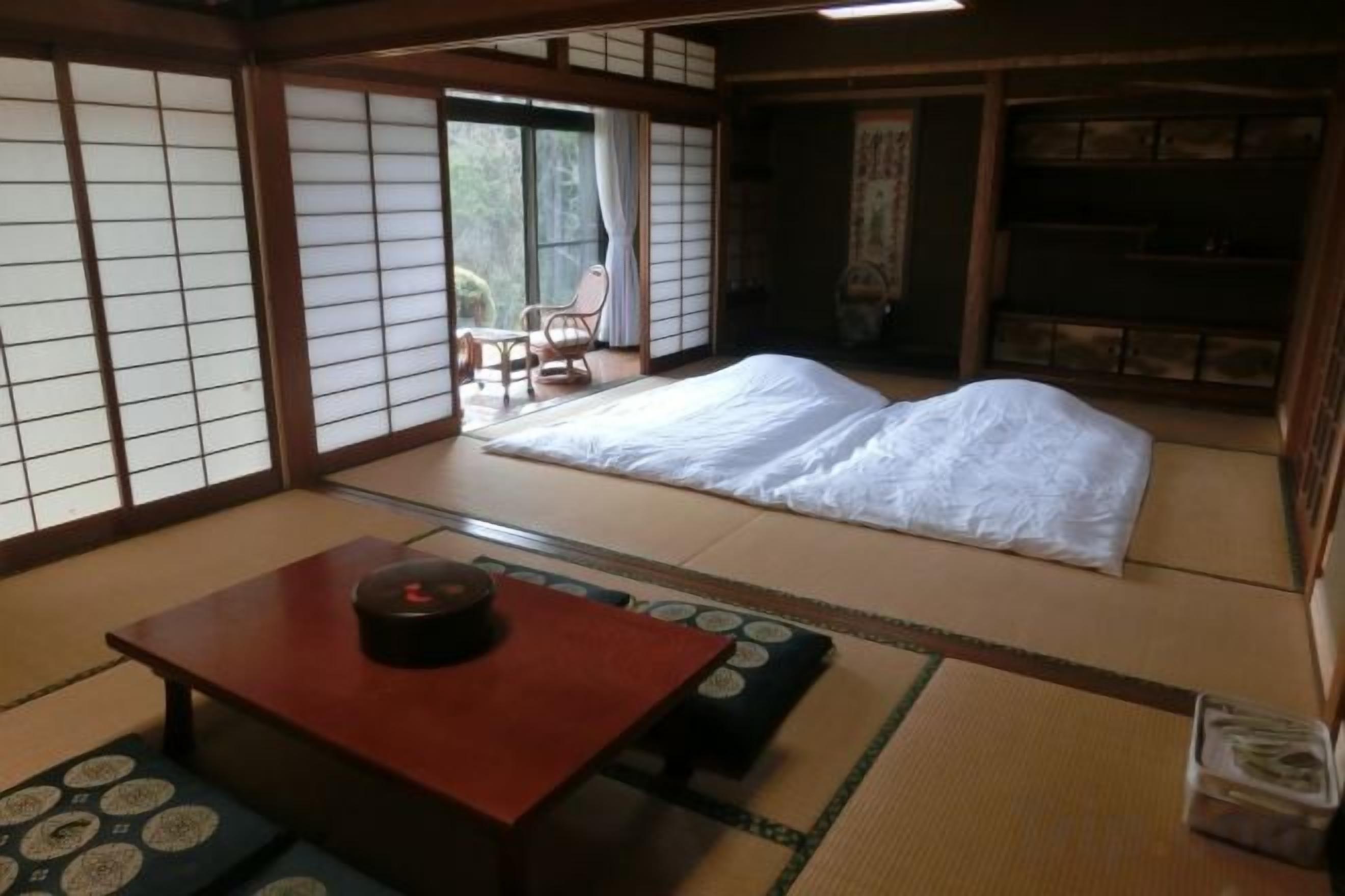 A traditional Japanese room with tatami flooring, a futon bed, a low wooden table, and sliding doors.