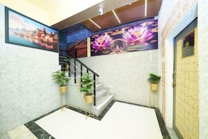 A hotel lobby with a staircase, a mural, and potted plants. - Golden Lotus (Varanasi)