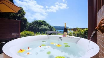A hot tub with water lilies and a bottle of champagne, set against a clear sky and a view of the sea.