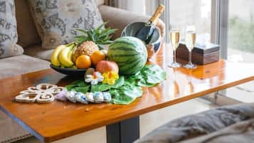 A wooden table with a fruit bowl, a bottle of champagne, and two glasses.