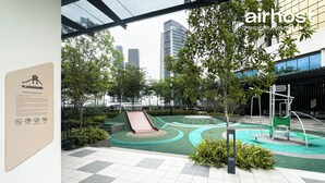 Ein Spielplatz mit Rutsche und Klettergerüsten, umgeben von Grünflächen und modernen Gebäuden im Hintergrund.