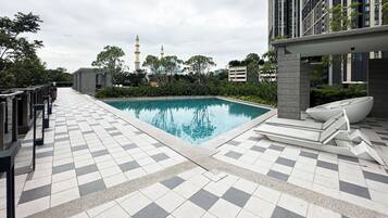 A modern hotel pool area with a tiled floor, a lounge chair, and a view of a mosque in the background.