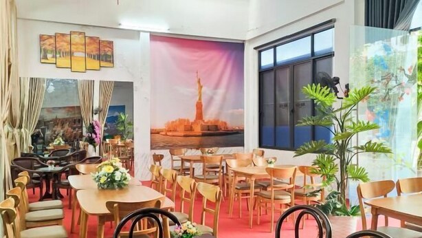 A dining area with wooden tables and chairs, a large window with a view, and a mural of a city skyline. - Chill Out (Vy Da)