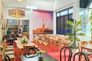 A dining area with wooden tables and chairs, a large window with a view, and a mural of a city skyline. - Chill Out (Vy Da)