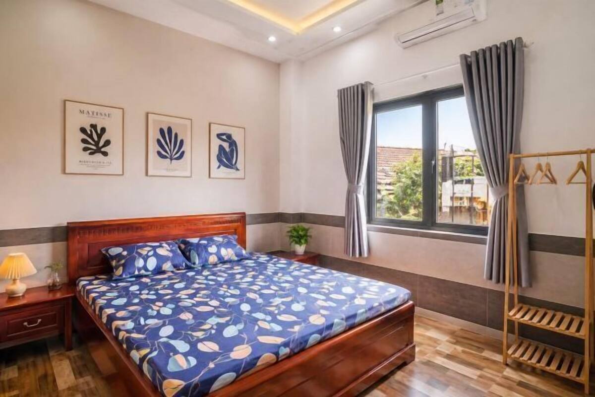 Une chambre à coucher avec un lit en bois, une table de chevet, une fenêtre avec des rideaux et des œuvres d’art murales.