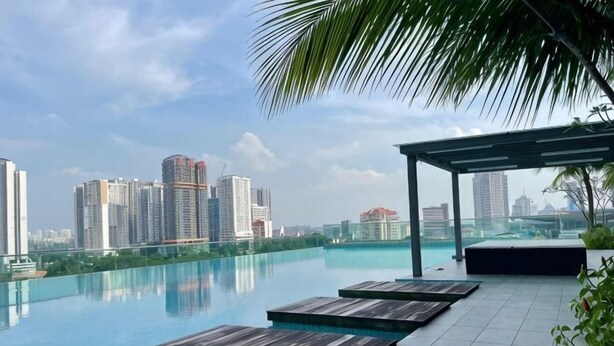 A rooftop infinity pool with wooden deck seating, a covered area, and a city skyline view. - Paragon Suites L18 By UCome Homestay (Johor Bahru)