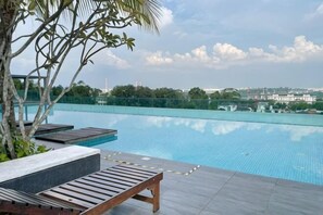 A swimming pool with lounge chairs, a palm tree, and a view of buildings in the background. - Paragon Suites L18 By UCome Homestay (Johor Bahru)