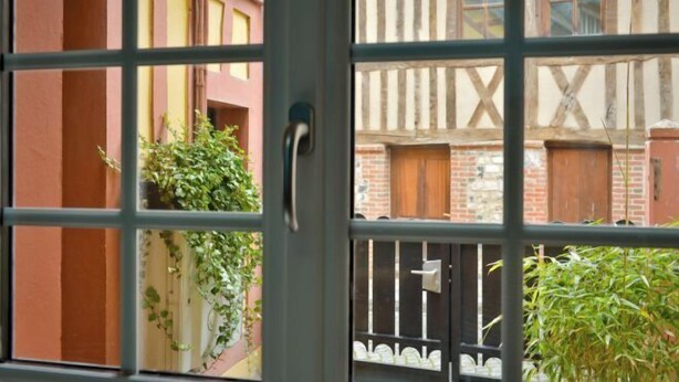 A view through a window with a grid pattern, revealing a building with exposed brick and wooden beams. - La Maison de Pierre et Valérie Saint Catherine (Honfleur)
