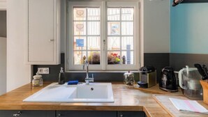 A kitchen with a white sink, a window with a view, and various kitchen items on the counter. - La Maison de Pierre et Valérie Saint Catherine (Honfleur)