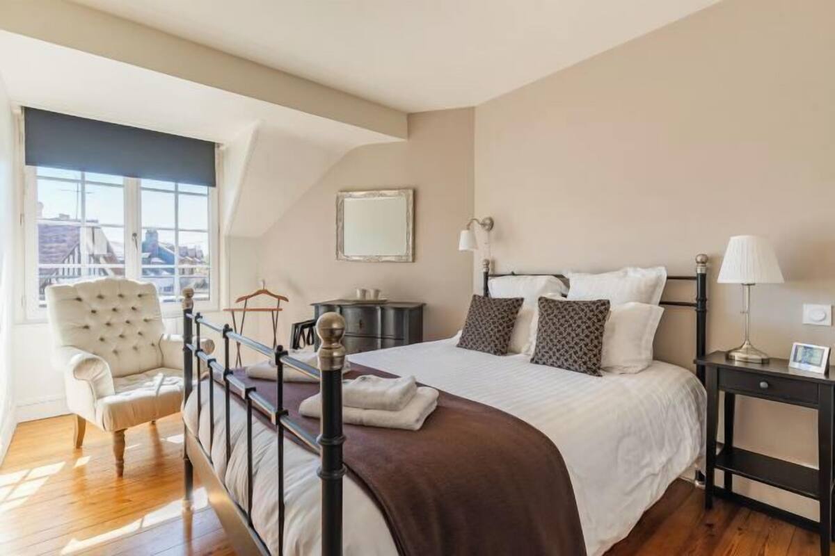 Quarto com cama, mesas de cabeceira, uma cadeira, janela e vista para a cidade.