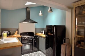 A compact kitchen with a stove, oven, and black refrigerator, a wooden countertop, and a patterned backsplash. - La Maison de Pierre et Valérie Saint Catherine (Honfleur)