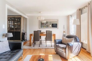 A living room with a sofa, a leather chair, a dining table with chairs, a TV, and a bookshelf. - La Maison de Pierre et Valérie Saint Catherine (Honfleur)