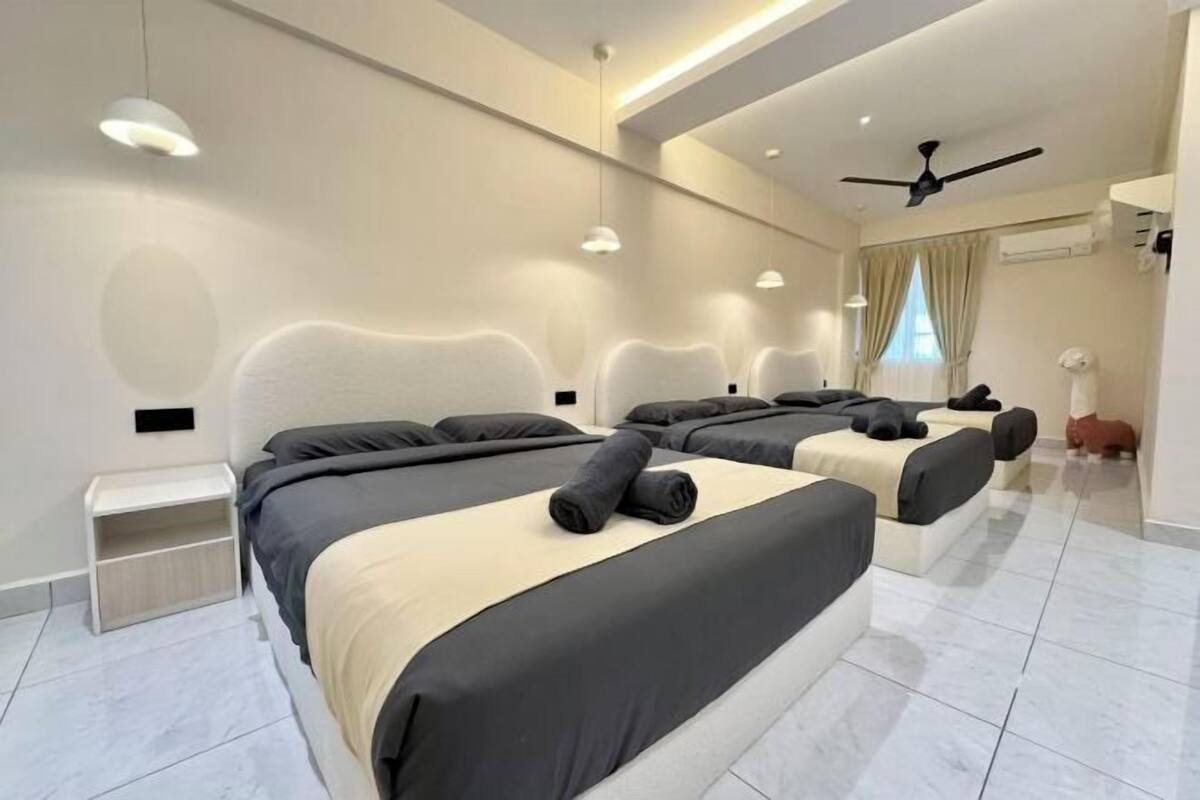 A modern hotel room with three beds, a ceiling fan, and a small seating area.