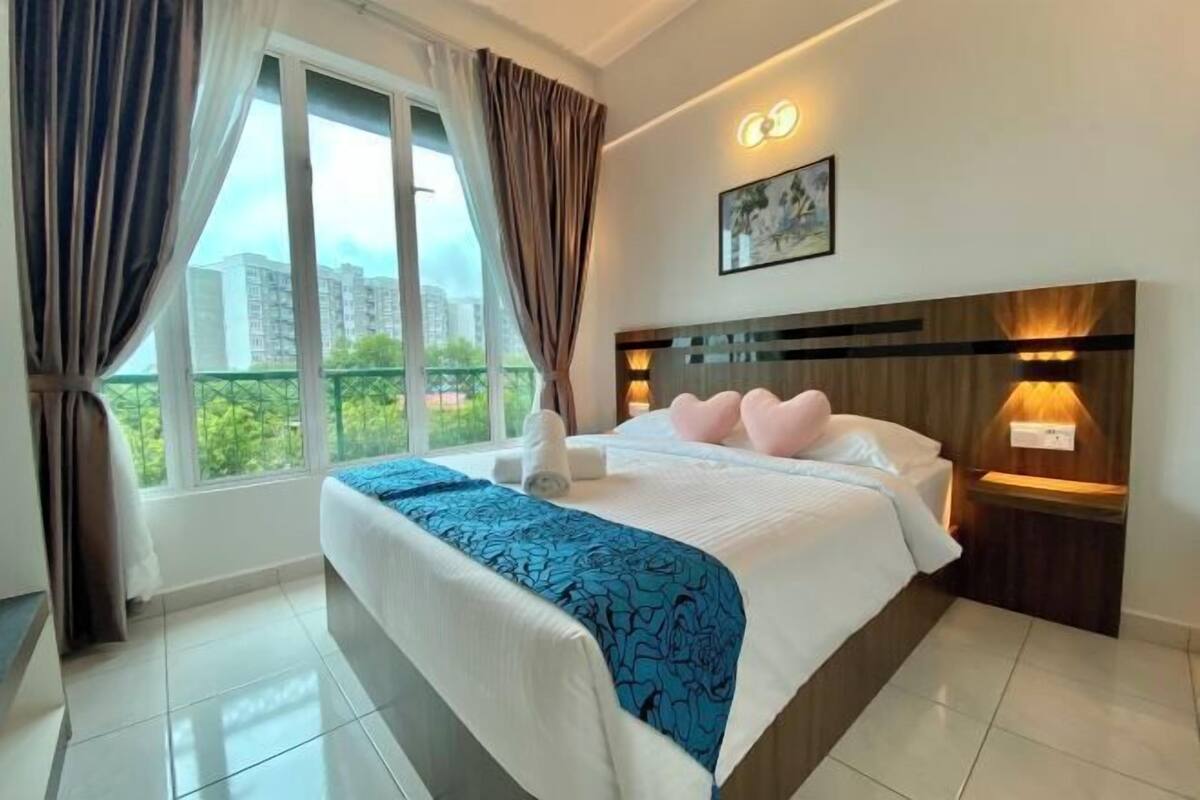 A hotel room with a large bed, a nightstand, a wall-mounted lamp, and a window with curtains.