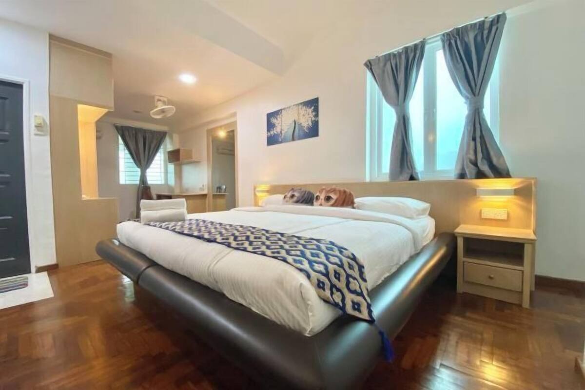 A modern bedroom with a large bed, a nightstand, a wall-mounted lamp, and a window with curtains.