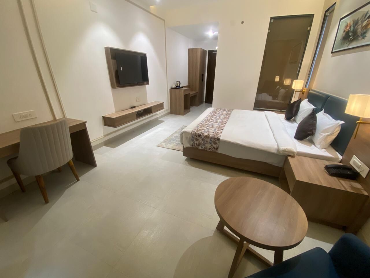 A modern hotel room with a bed, bedside tables, a TV, and a small round table.