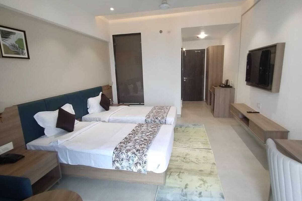 A modern hotel room with two beds, a desk, a TV, and a bathroom visible through an open door.
