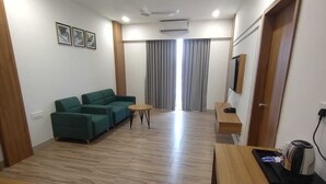 A modern hotel room with a green sofa set, a small round table, and a wooden desk with a kettle. - Hotel Swastik inn By Nexottel (Khambhaliya)