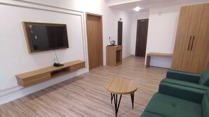 A spacious living area with a flat-screen TV mounted on the wall, a wooden coffee table, and a green sofa. - Hotel Swastik inn By Nexottel (Khambhaliya)