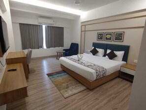 Quarto de hotel moderno com uma cama grande, uma escrivaninha, uma cadeira e uma televisão.