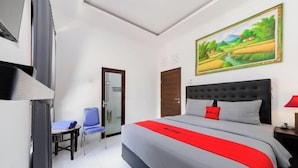 A hotel room with a large bed, a chair, a desk, and a painting on the wall. - RedDoorz @ Lotus House Seminyak (Bali)