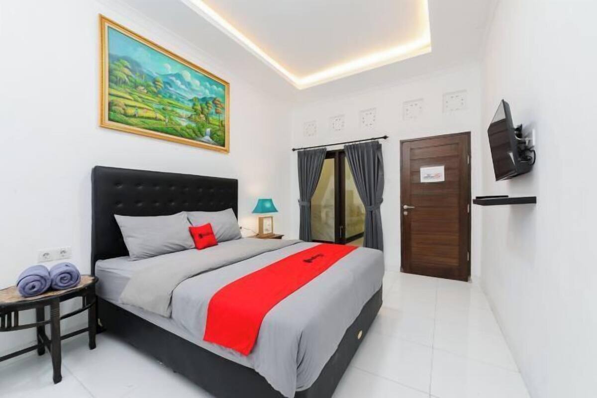 A bedroom with a bed, a painting, a TV, and a door.
