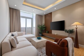 A modern living room with a sofa, a coffee table, a TV, and a lamp. - Chic Downtown Living w Dubai Cityscape Views (Dubai)