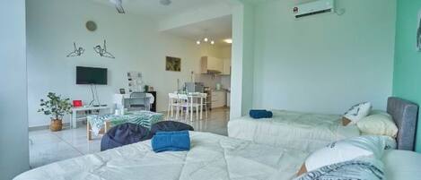 A hotel room with two beds, a TV, a ceiling fan, and a kitchenette in the background.