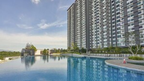 A modern high-rise building with a large, clear swimming pool in the foreground.