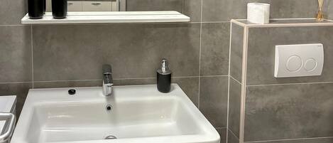 A bathroom with a white sink, a mirror, and a towel rack. There is a shelf with toiletries and a tissue box.