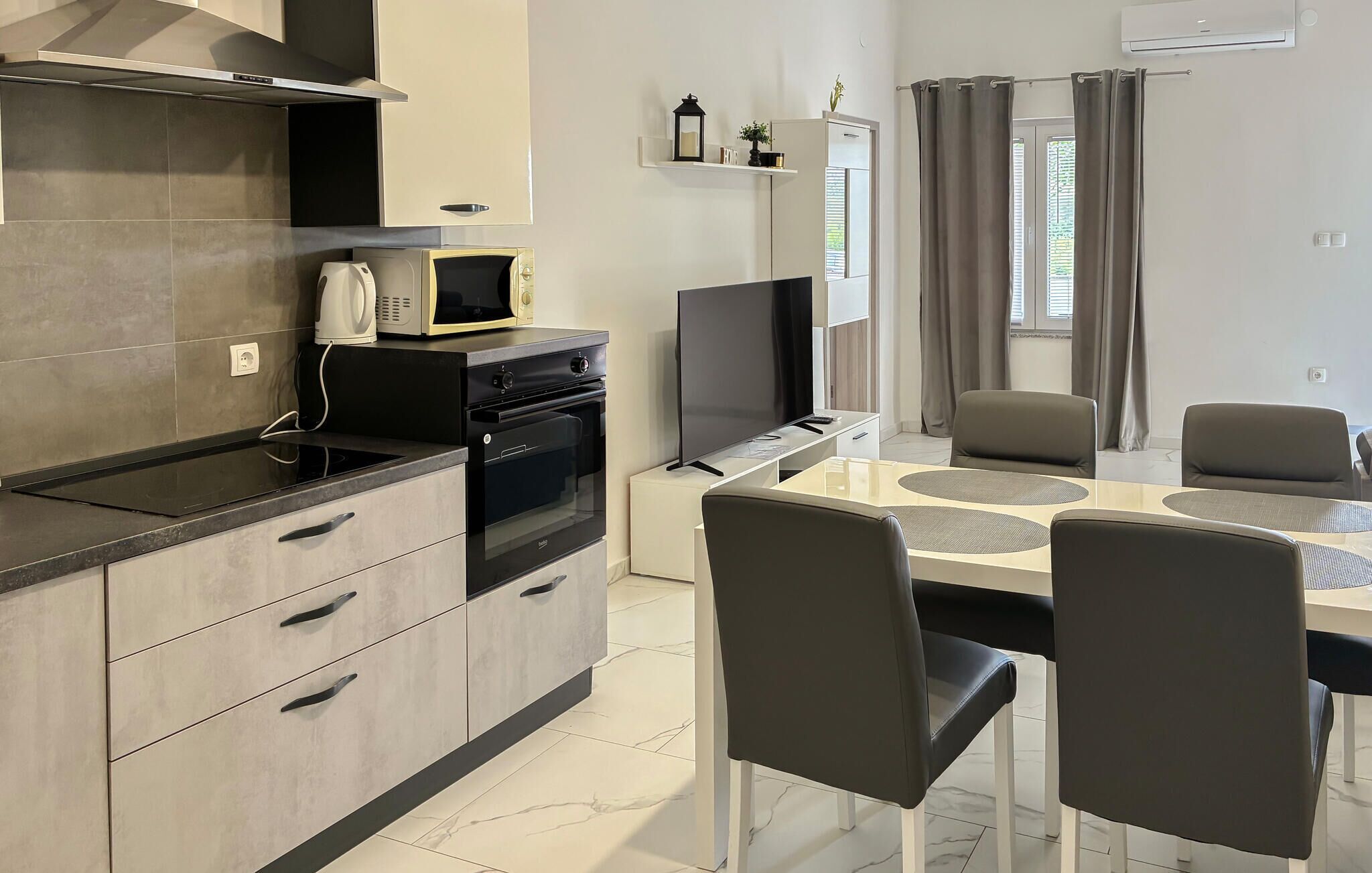 Eine moderne Küche mit Mikrowelle, Backofen und Herd, ein Essbereich mit Tisch und Stühlen sowie ein Fenster mit Vorhängen.