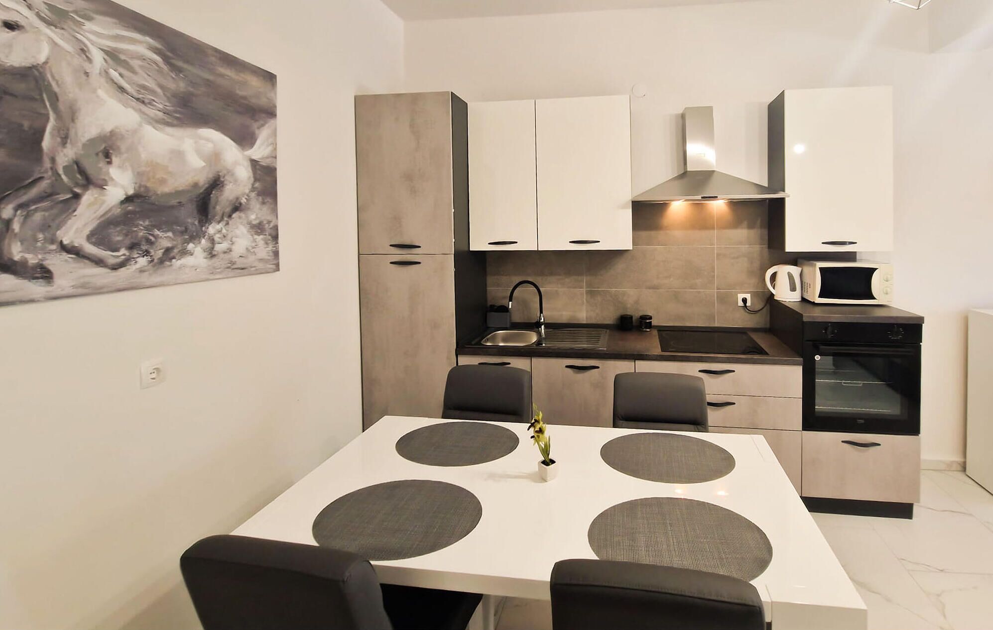 Una cocina moderna con comedor, que presenta una mesa blanca con individuales grises, sillas negras y un cuadro en la pared.