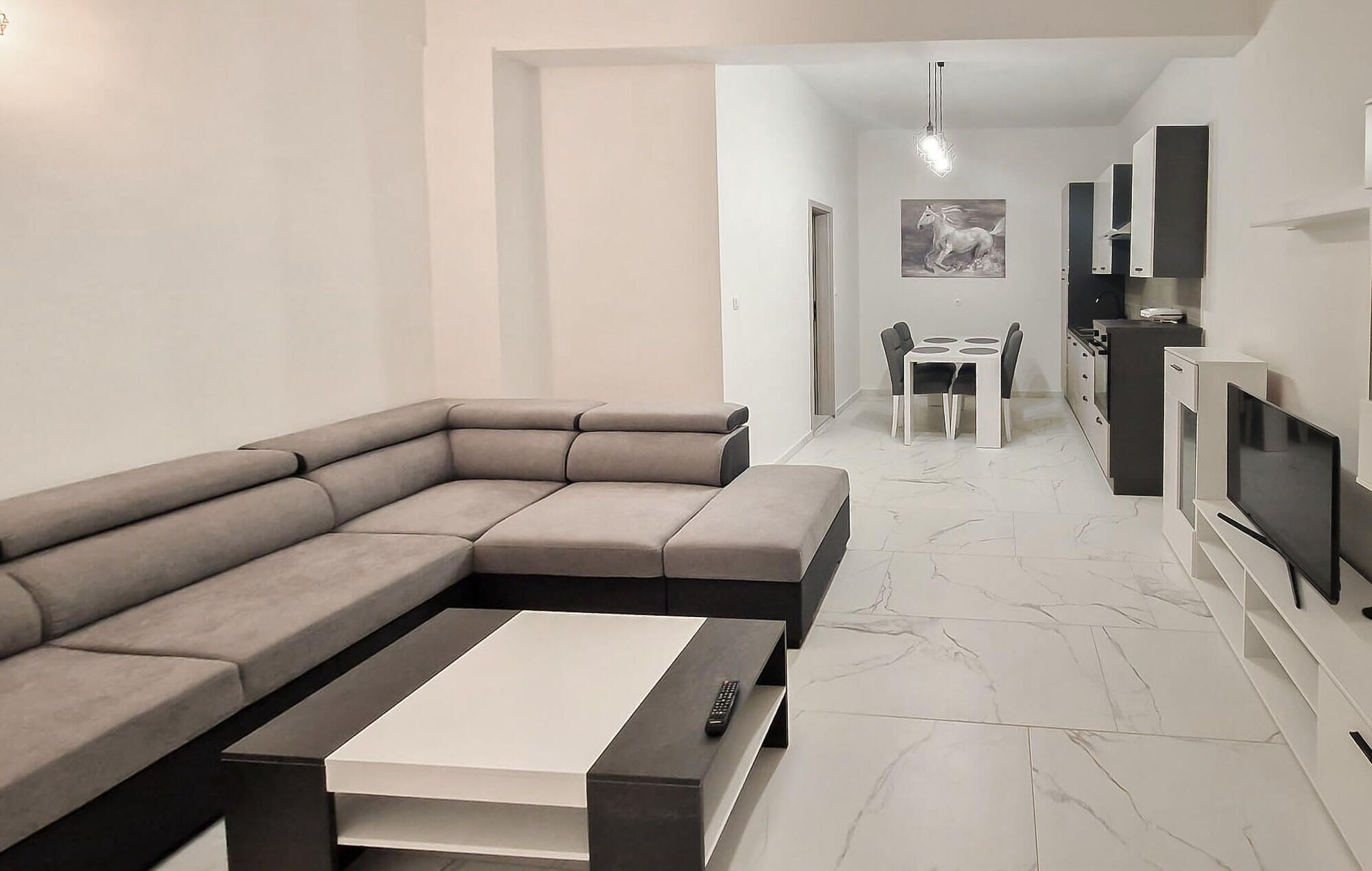 Een moderne woonkamer met een hoekbank, een salontafel, een eethoek met een tafel en stoelen, en een keuken met een televisie en kastjes.