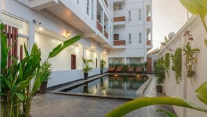 Un patio de hotel con piscina, plantas en macetas y un edificio de varios pisos con balcones.