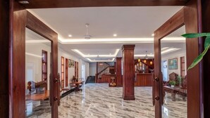 Un vestíbulo con suelo de mármol, puertas de madera, una escalera y un mostrador de recepción.